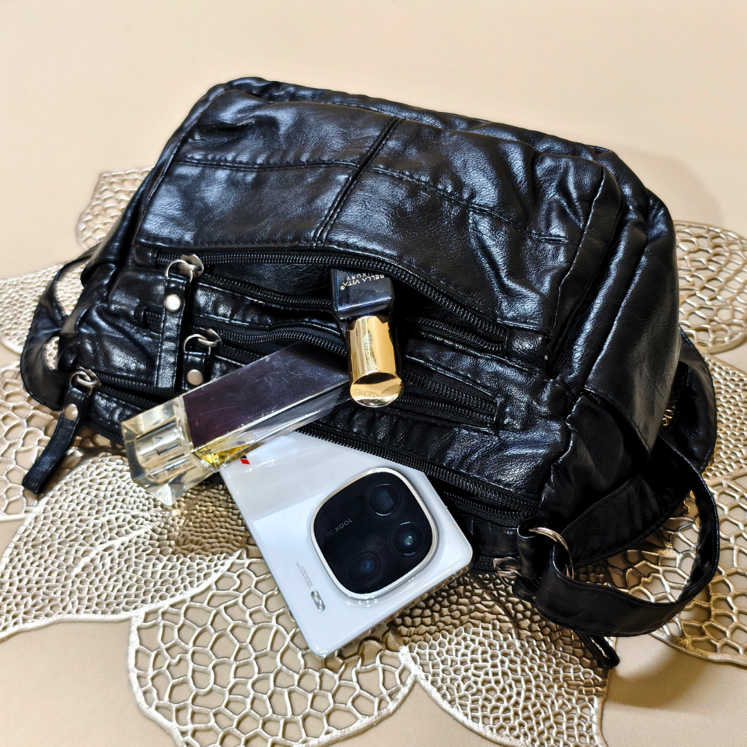 Black leather bag with a phone and lipstick on a textured surface