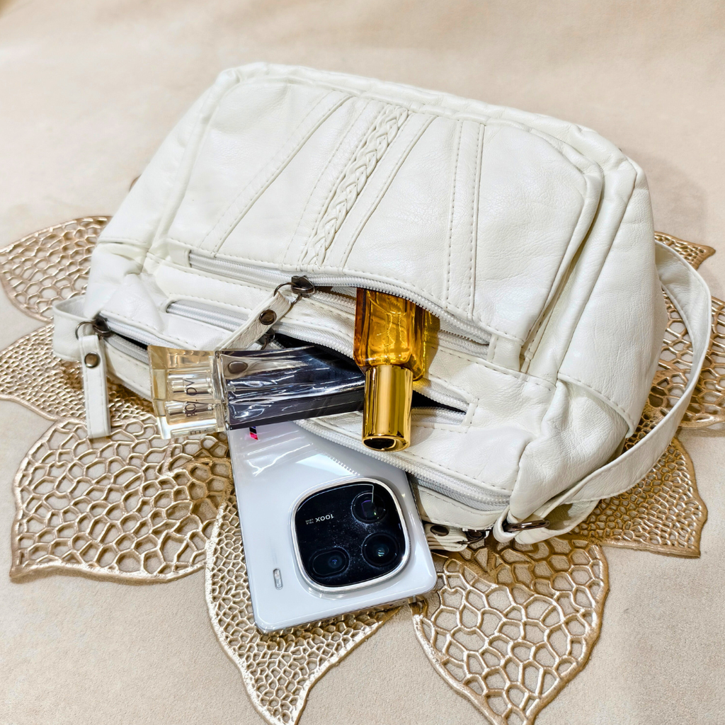 White handbag with a phone, perfume bottle, and other items on a decorative mat.
