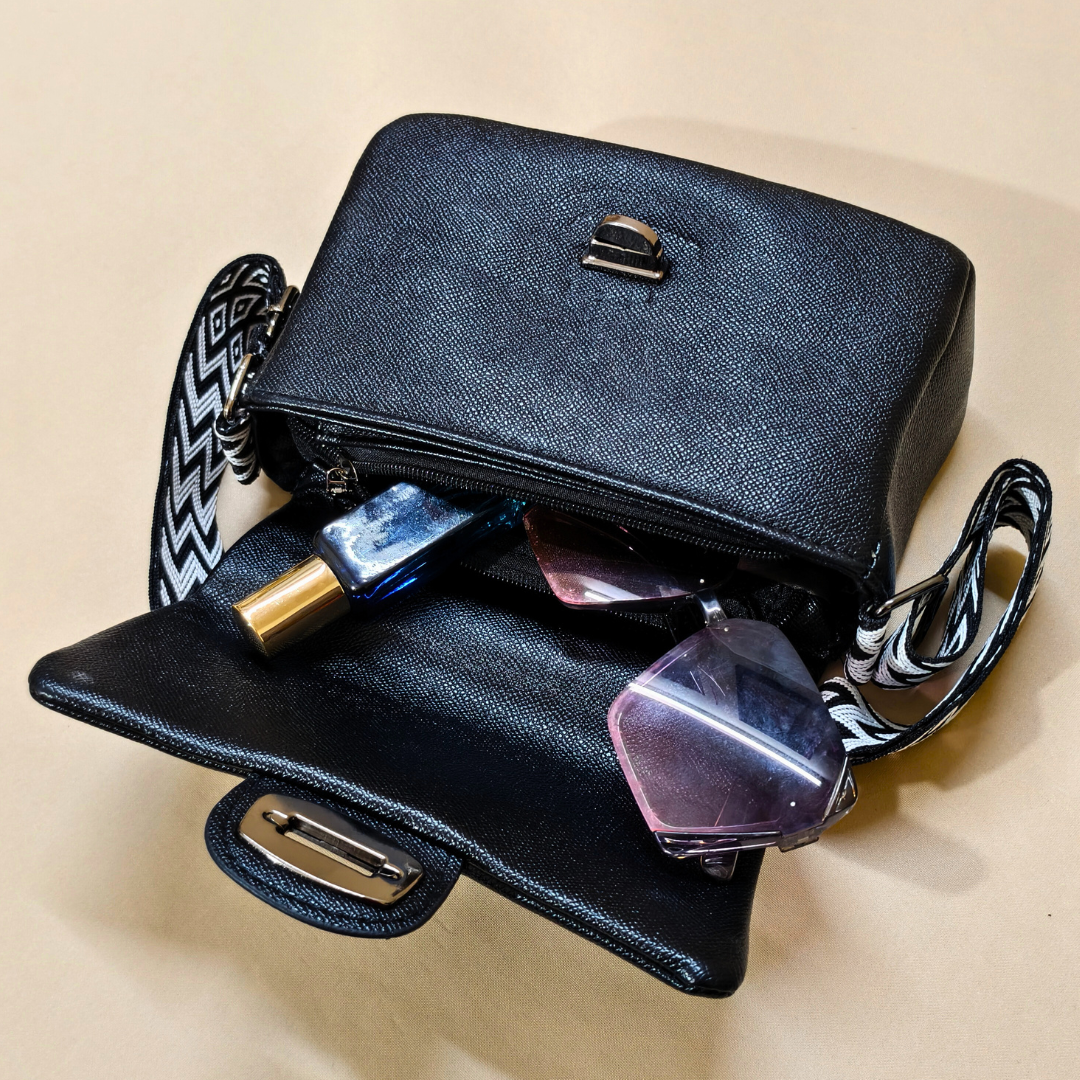 Black handbag with sunglasses and a bottle on a beige background