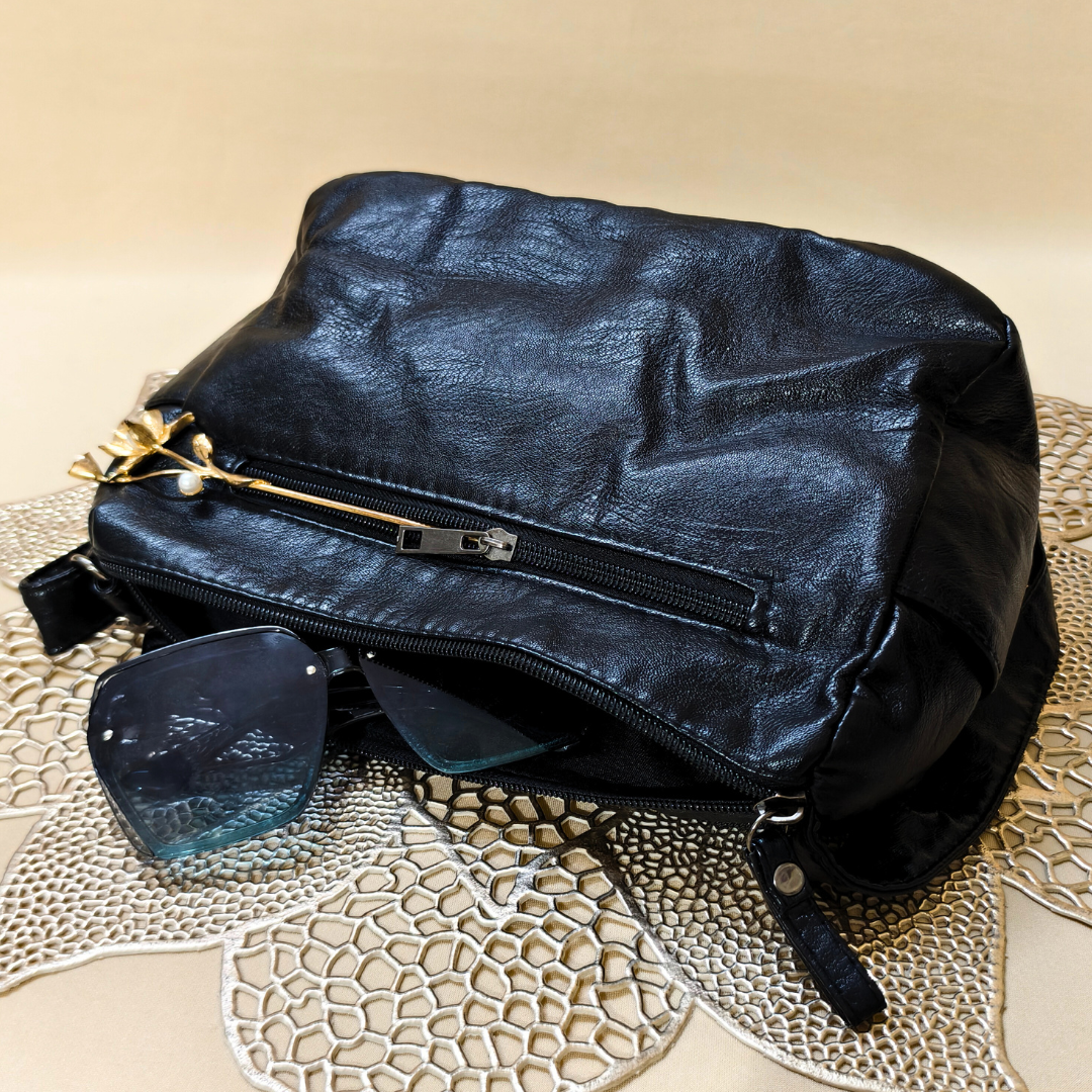 Black leather bag with sunglasses on a textured beige surface