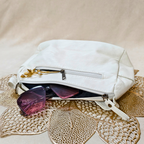 White handbag with sunglasses on a textured beige surface