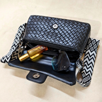 Black woven handbag with a patterned strap, containing a bottle and sunglasses on a beige background.
