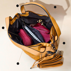 Open tan leather bag with a pink pouch and notebook on a beige background