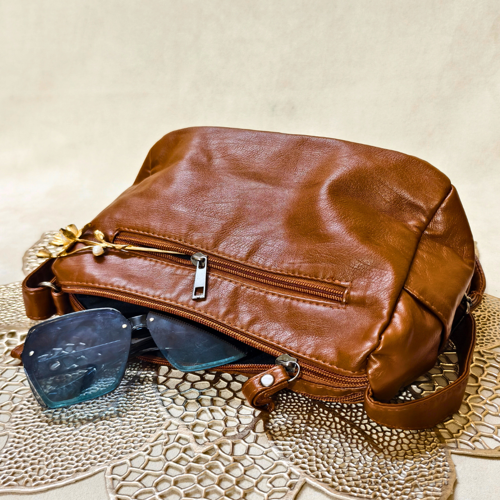 Brown leather bag with sunglasses on a textured surface