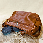 Brown leather bag with sunglasses on a textured surface