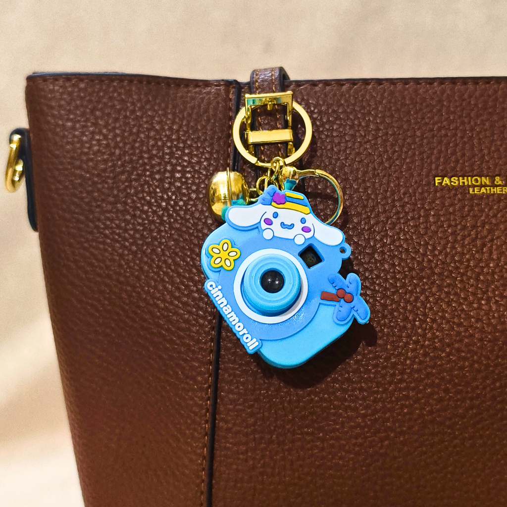 Blue camera-shaped keychain with cartoon design on a brown leather bag.