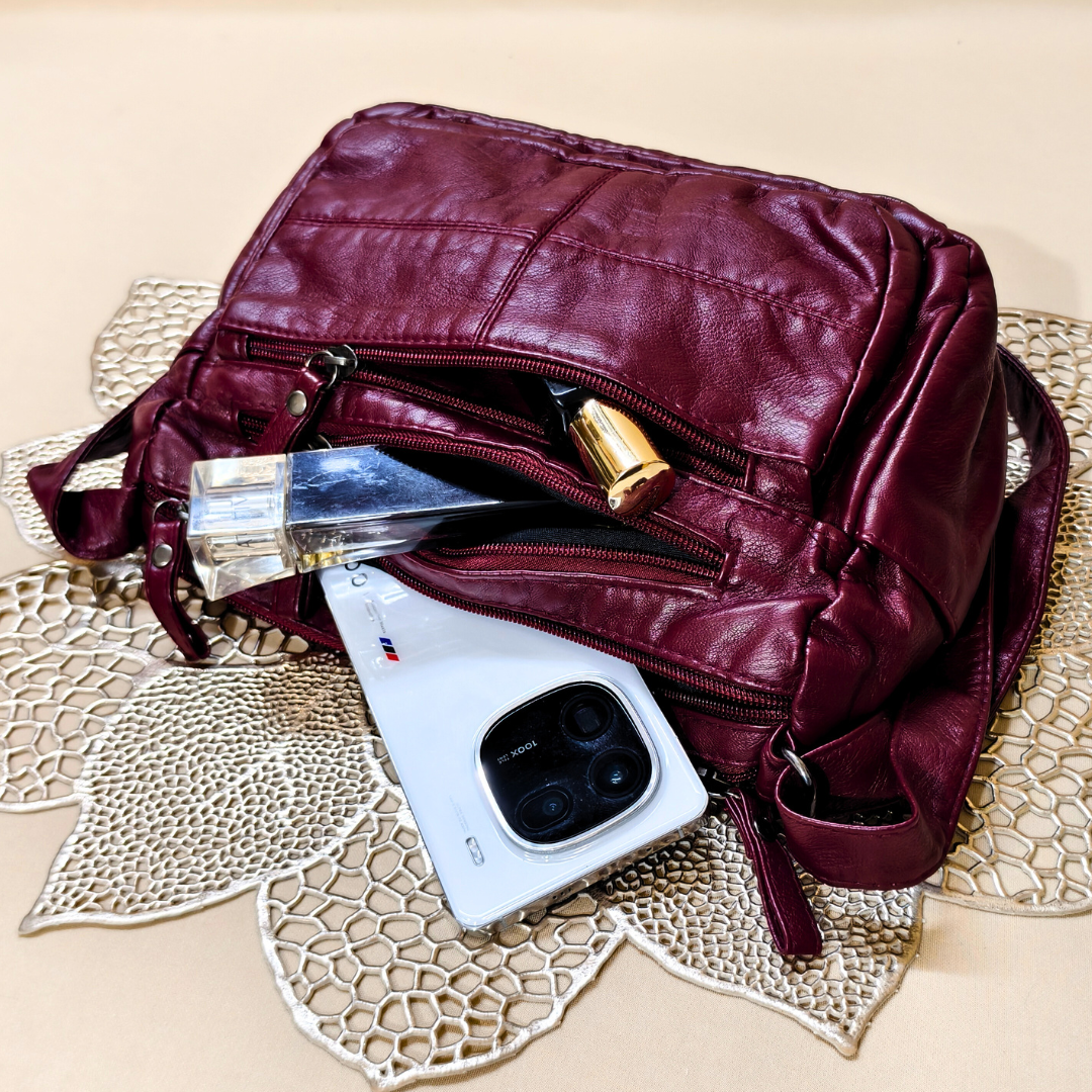 Maroon leather bag with a phone and camera inside on a textured surface