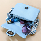 Light blue handbag with sunglasses and a blue bottle on a beige background