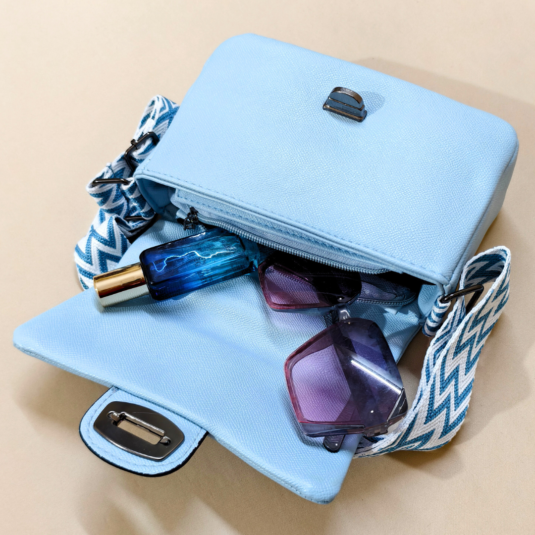 Light blue handbag with sunglasses and a blue bottle on a beige background