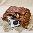 Brown leather clutch bag with items on a textured surface