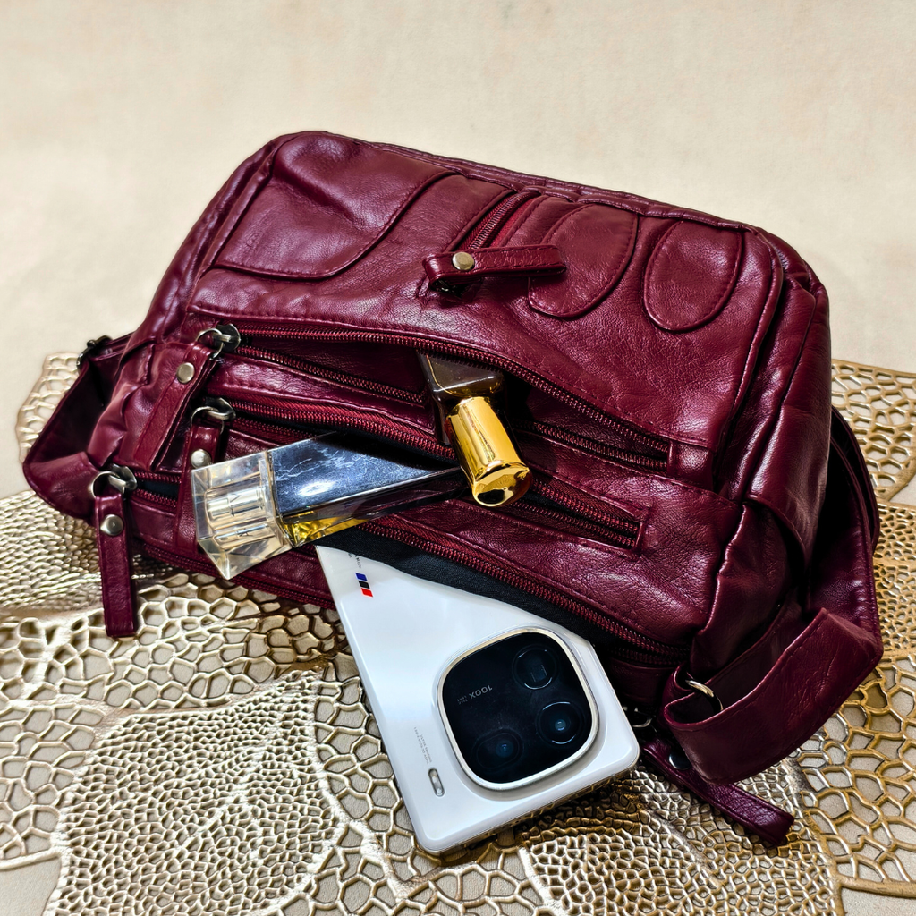 Maroon leather bag with cosmetic items on a textured surface