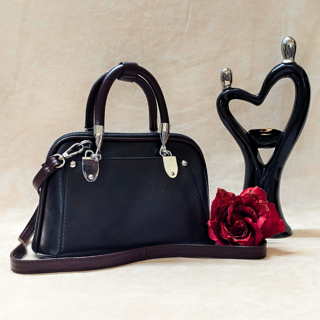 Black handbag with silver hardware, red rose, and black heart-shaped holder on beige background