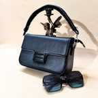 Black handbag with decorative handle featuring an angel figure, accompanied by a pair of sunglasses on a light background.