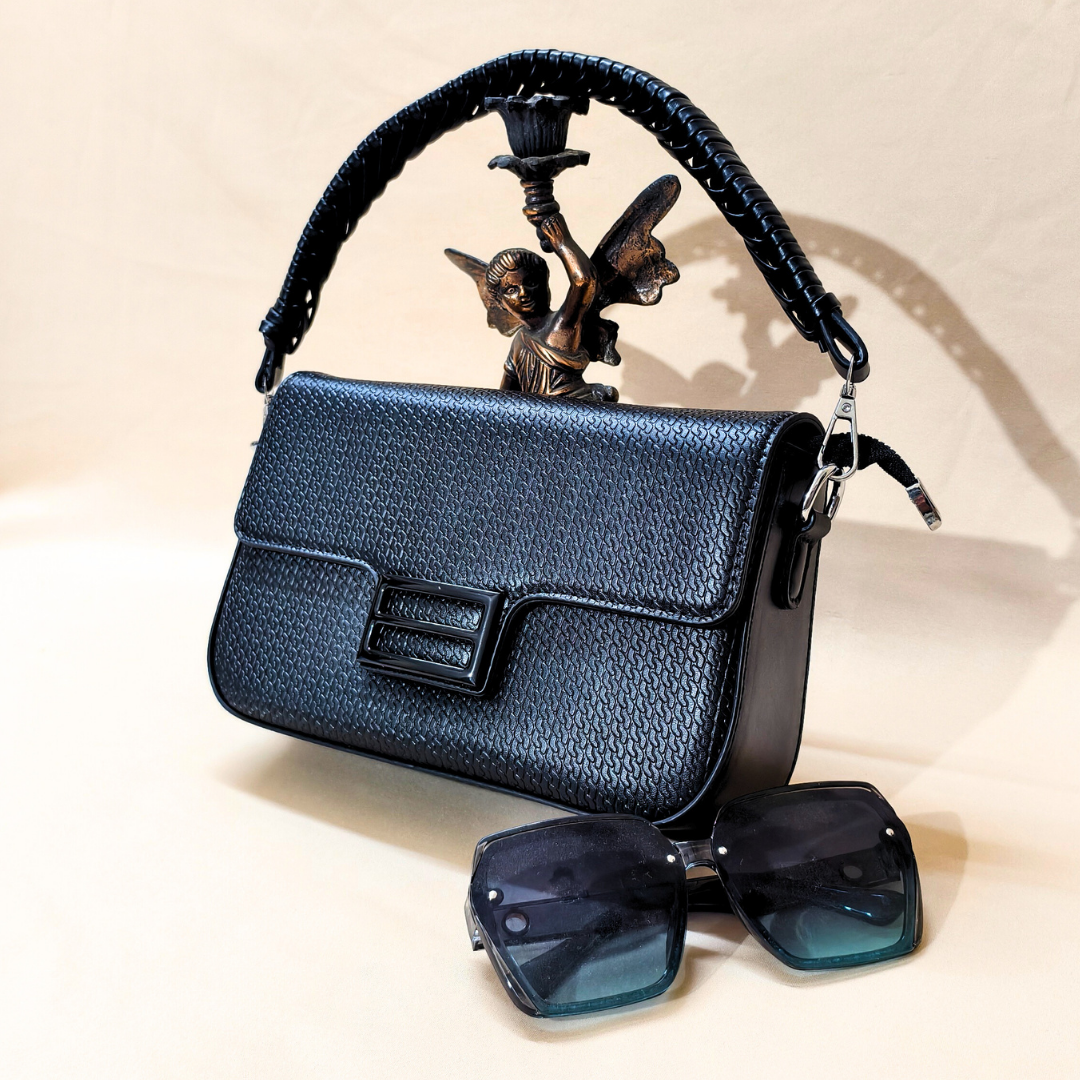 Black handbag with decorative handle featuring an angel figure, accompanied by a pair of sunglasses on a light background.