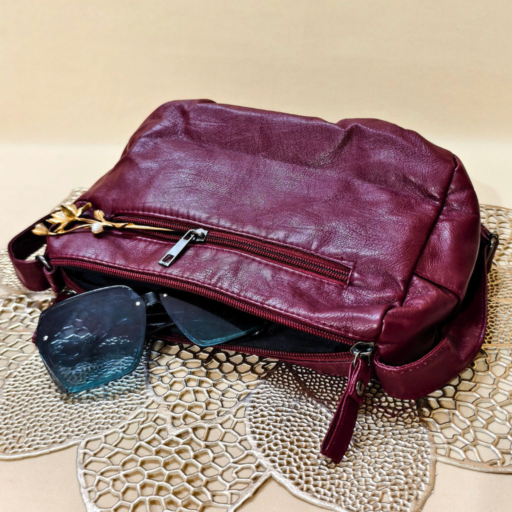 Maroon leather handbag with sunglasses on a textured surface