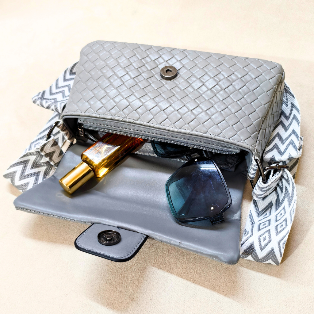 Gray woven handbag with sunglasses and a bottle on a beige background