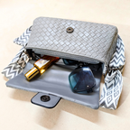 Gray woven handbag with sunglasses and a bottle on a beige background