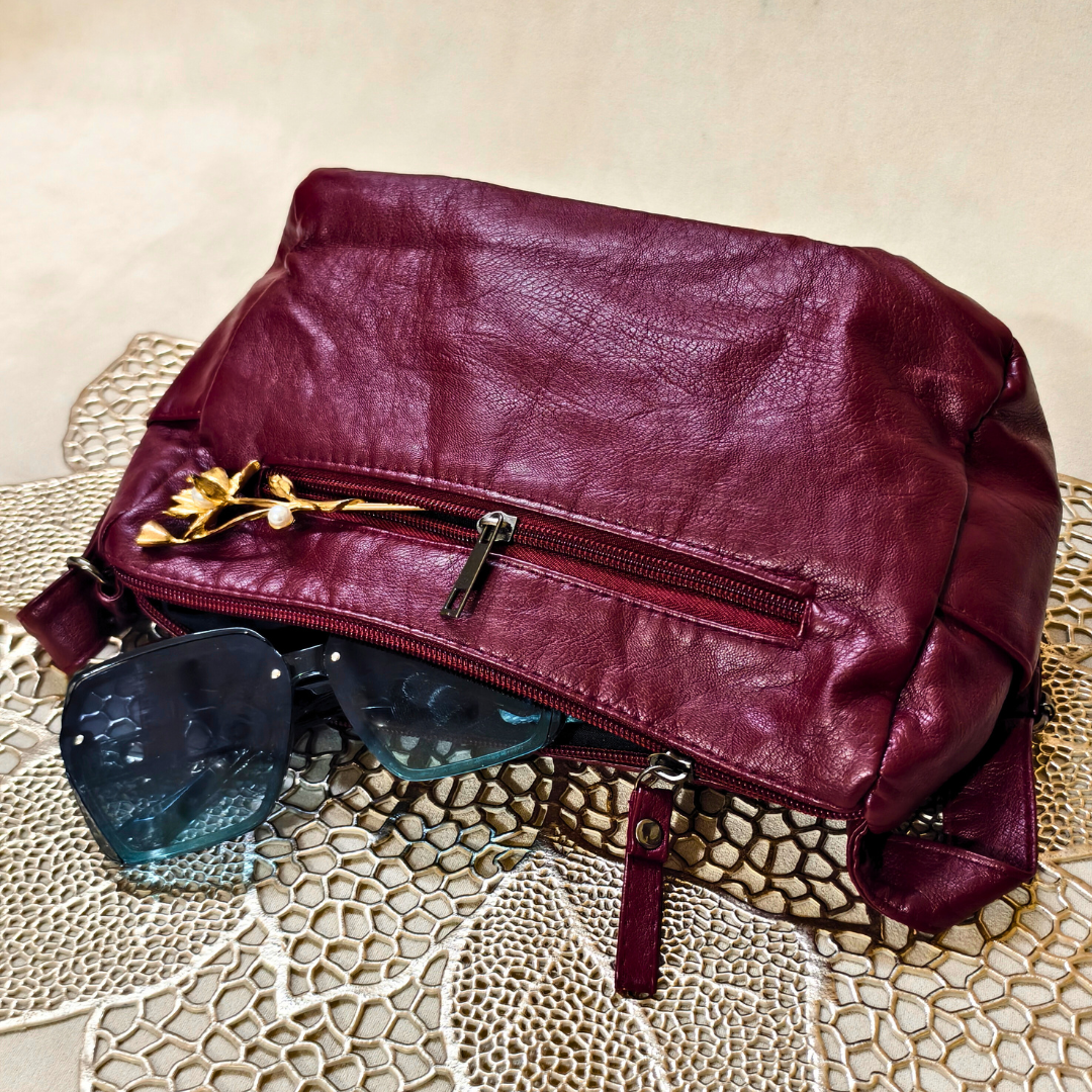 Maroon leather bag with sunglasses on a textured surface