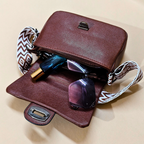Brown leather handbag with sunglasses and a bottle on a beige background