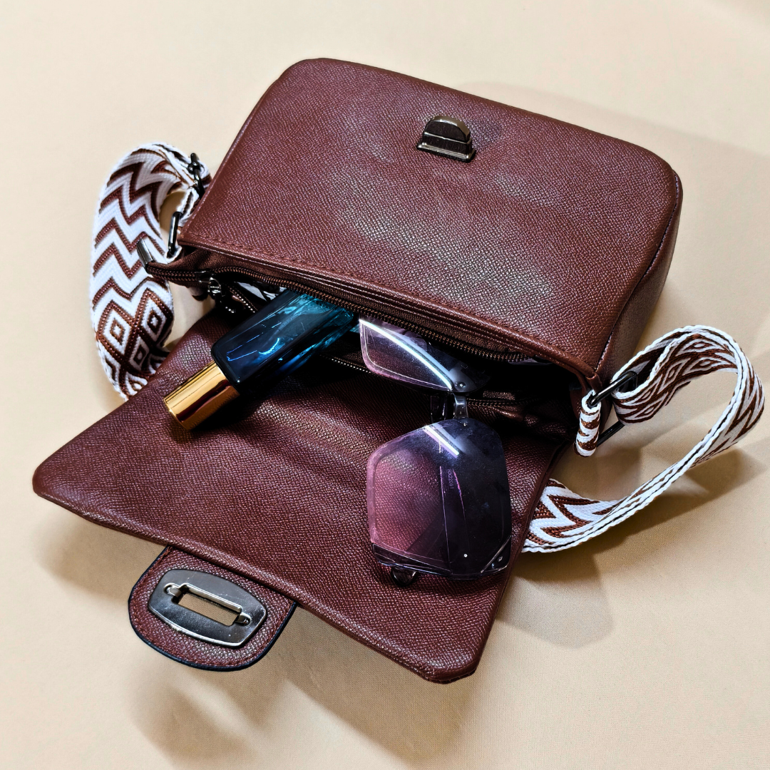 Brown leather handbag with sunglasses and a bottle on a beige background