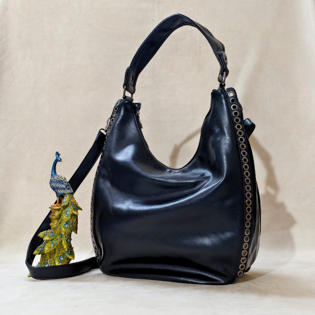 Black leather handbag with decorative peacock charm on a beige background