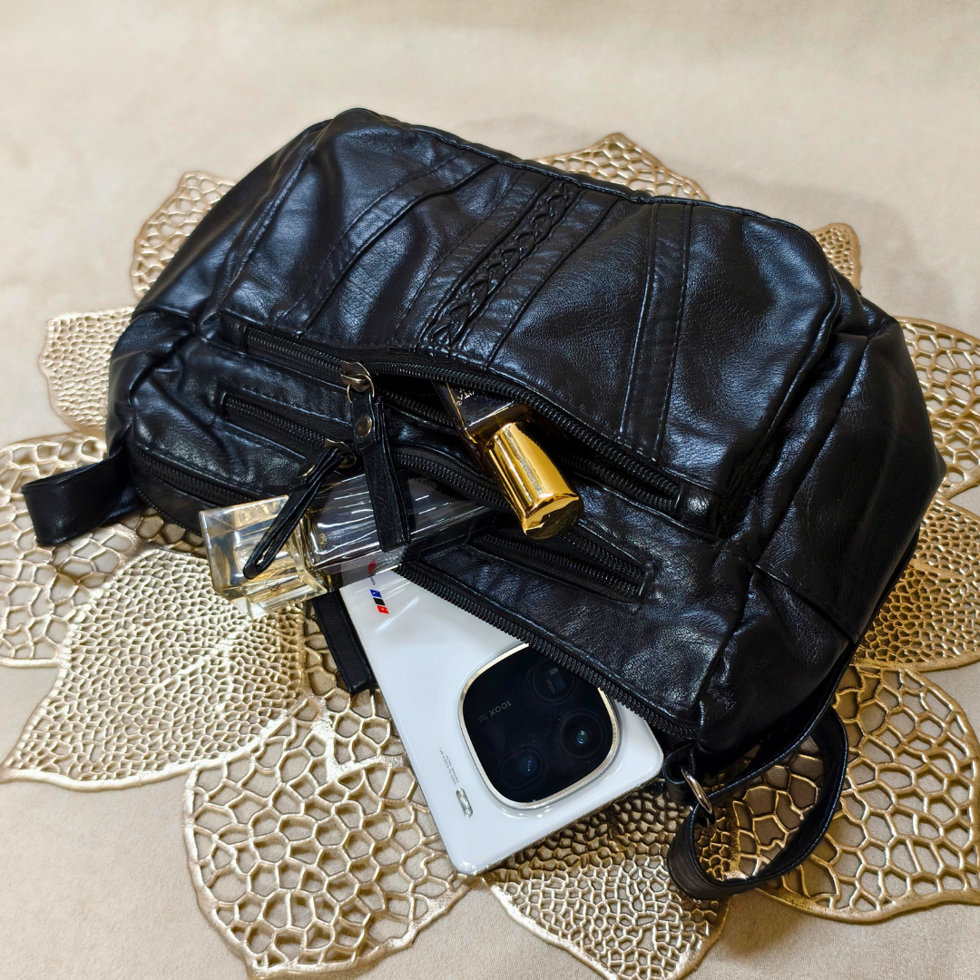 Black leather bag with a phone and perfume bottle on a decorative mat
