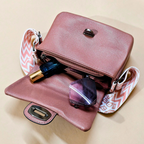 Pink handbag with cosmetic items on a beige background