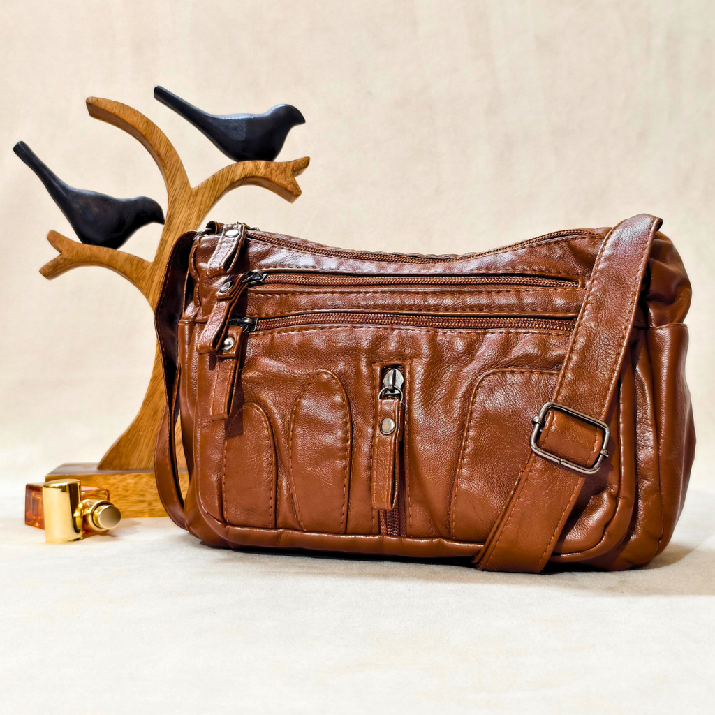 Brown leather handbag with multiple zippers on a beige background