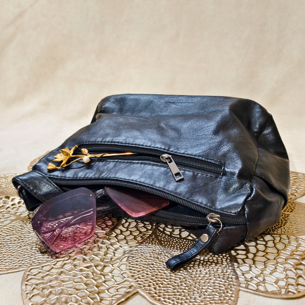 Black leather pouch with sunglasses on a textured beige surface