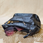 Black leather pouch with sunglasses on a textured beige surface