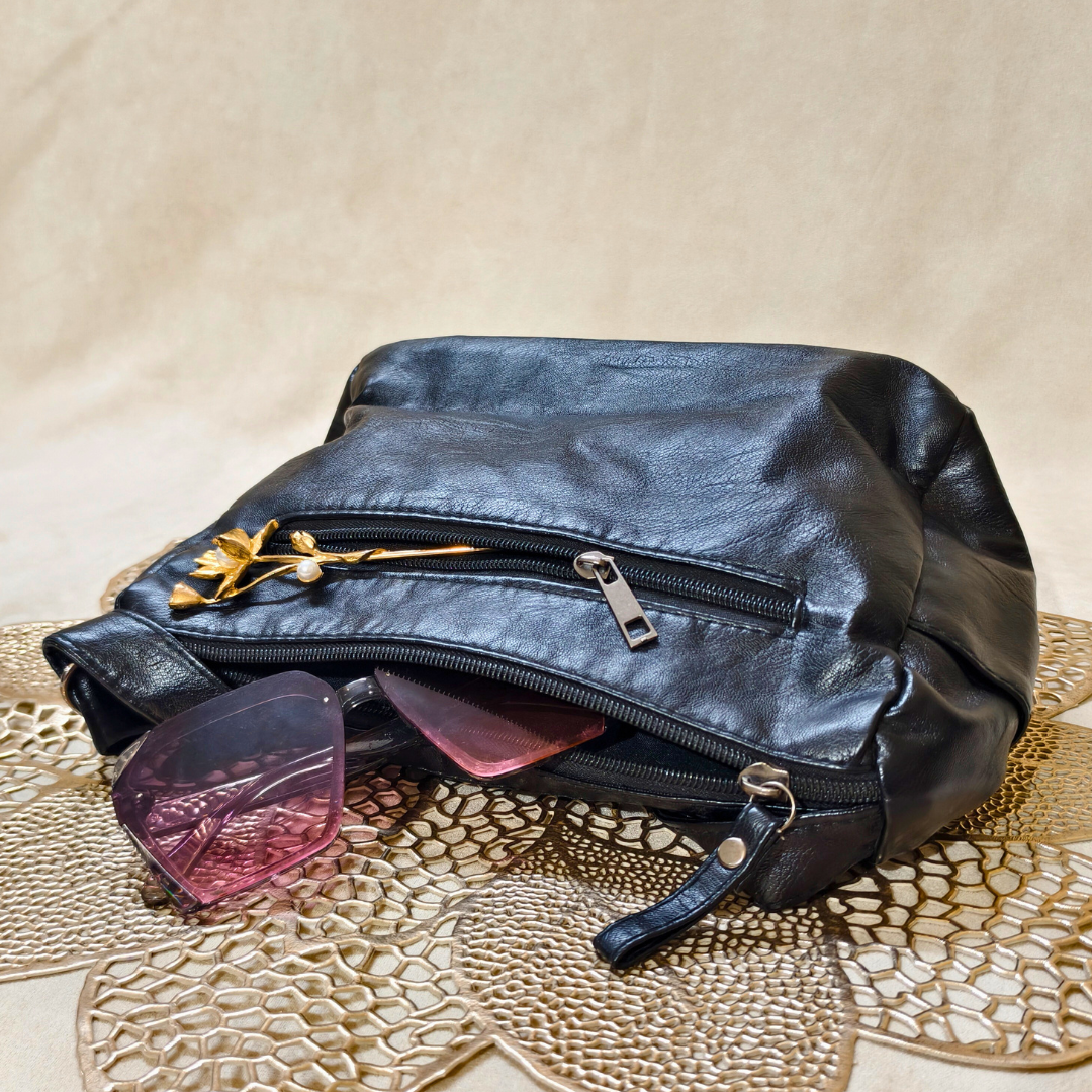 Black leather pouch with sunglasses on a textured beige surface