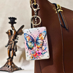 Colorful butterfly keychain attached to a brown leather bag with a statue in the background.