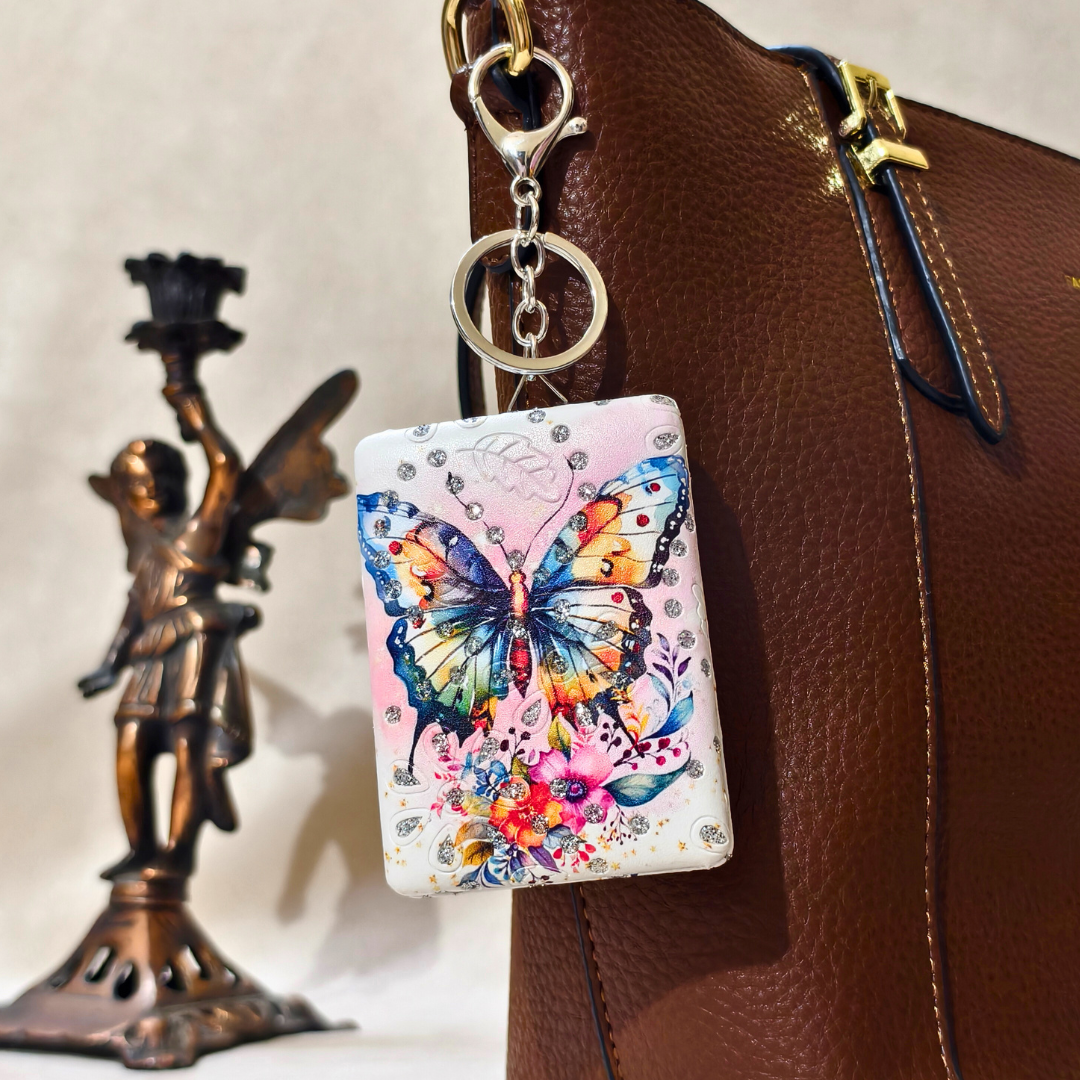 Colorful butterfly keychain attached to a brown leather bag with a statue in the background.