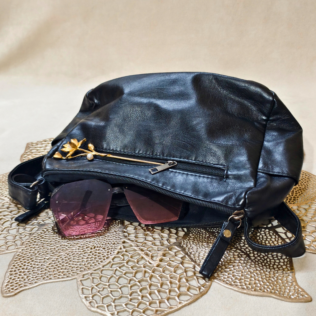 Black leather bag with sunglasses on a textured beige surface