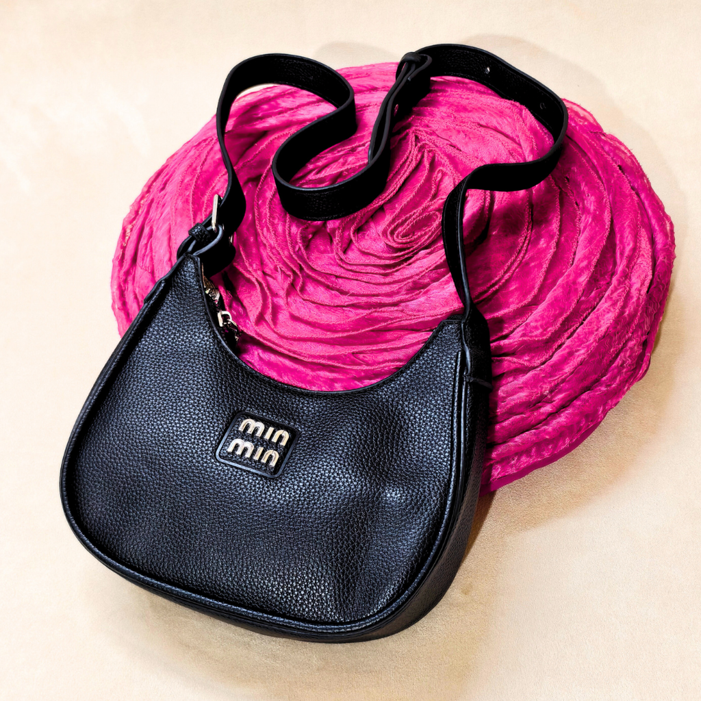 Black handbag with a visible brand logo on a pink textured background