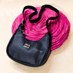Black handbag with a visible brand logo on a pink textured background