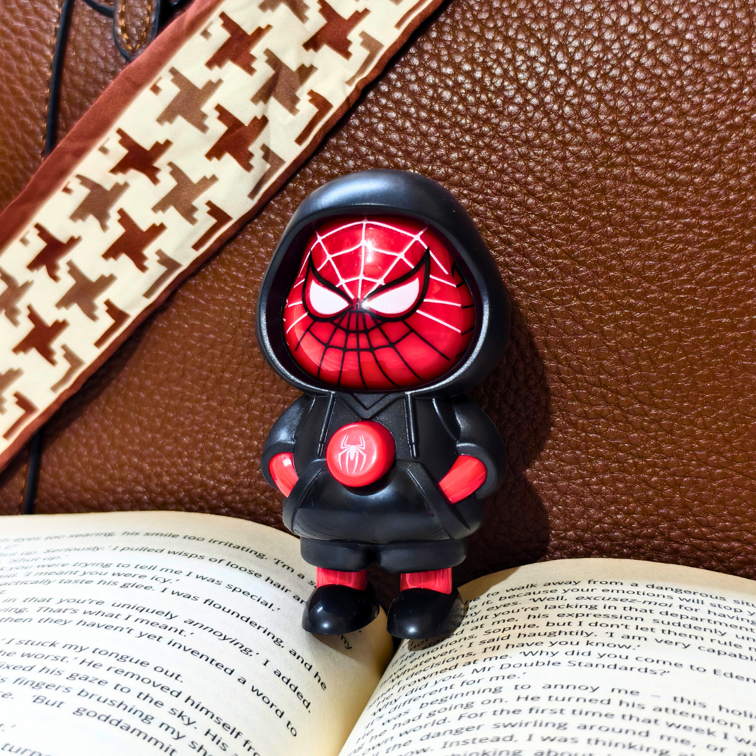 Spider-Man figurine on an open book with a brown leather surface and patterned strap in the background.