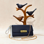 Navy blue handbag with gold chain and white strap in front of a wooden bird stand on a beige background
