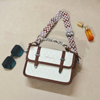 White and brown handbag with a zigzag strap, sunglasses, and a perfume bottle on a beige background