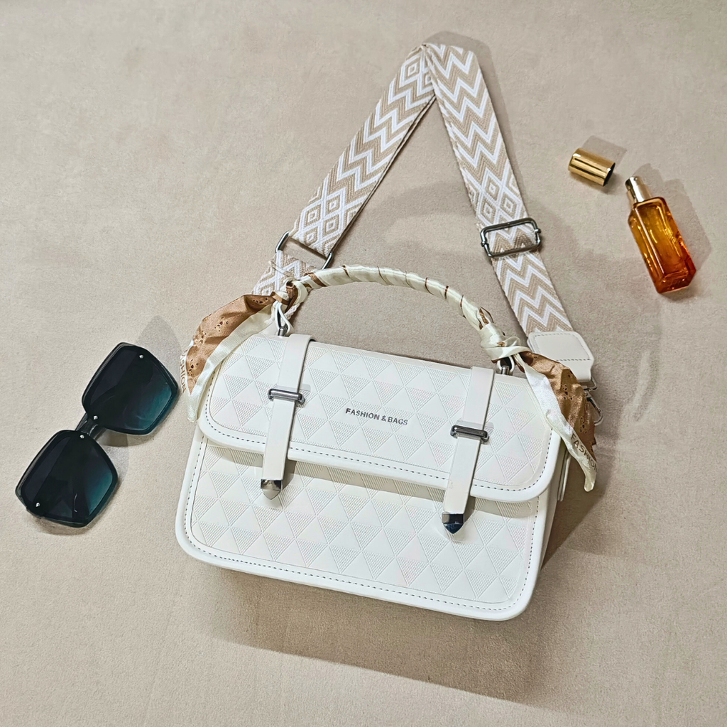 White quilted handbag with a patterned strap, accompanied by sunglasses and a perfume bottle on a beige surface.