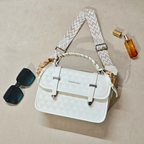 White quilted handbag with a patterned strap, accompanied by sunglasses and a perfume bottle on a beige surface.