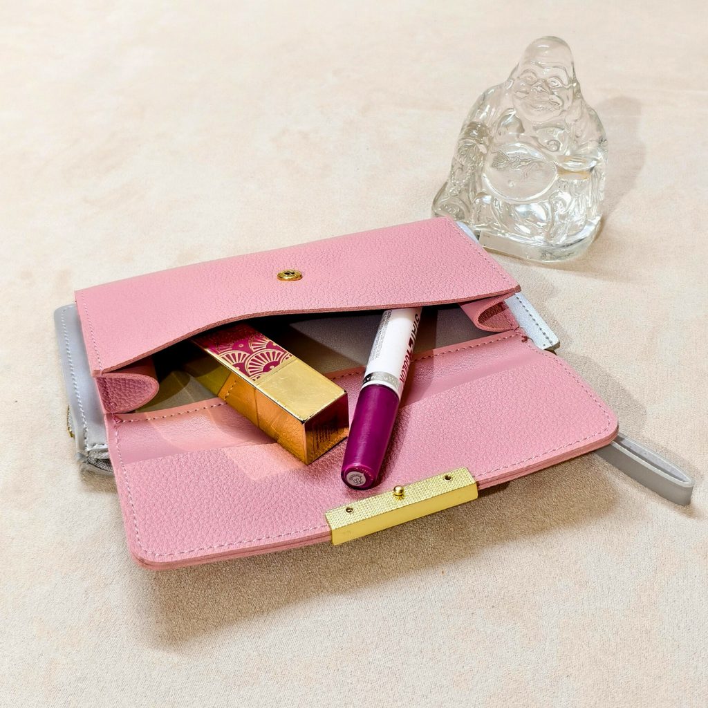 Pink makeup pouch with lipsticks and a brush on a beige surface