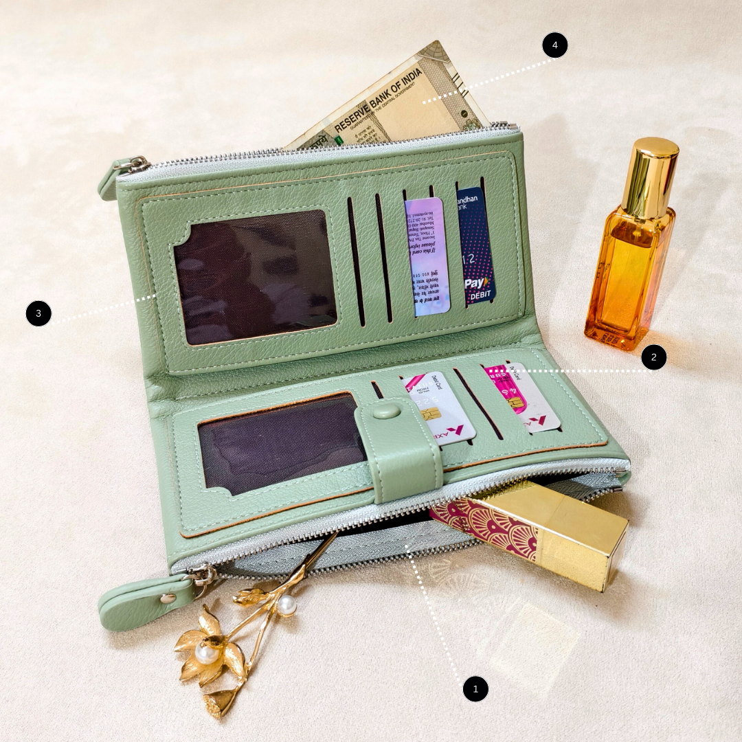 Green wallet with card slots and a phone holder, next to a bottle of perfume and a gold flower on a light background.
