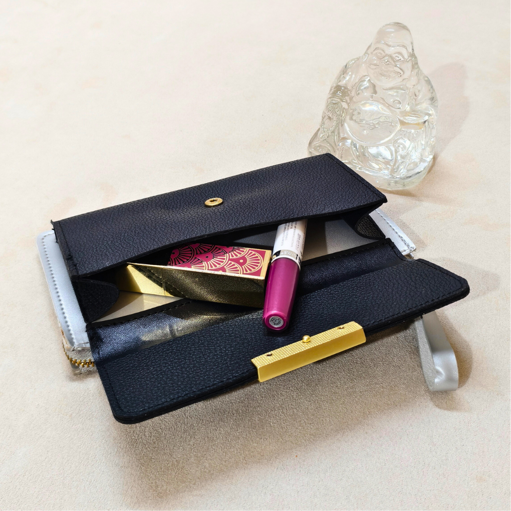 Black leather clutch with makeup items on a beige surface