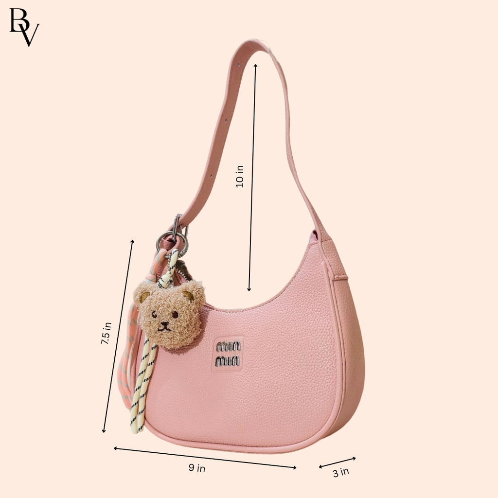 Pink handbag with a teddy bear keychain and measurements on a beige background