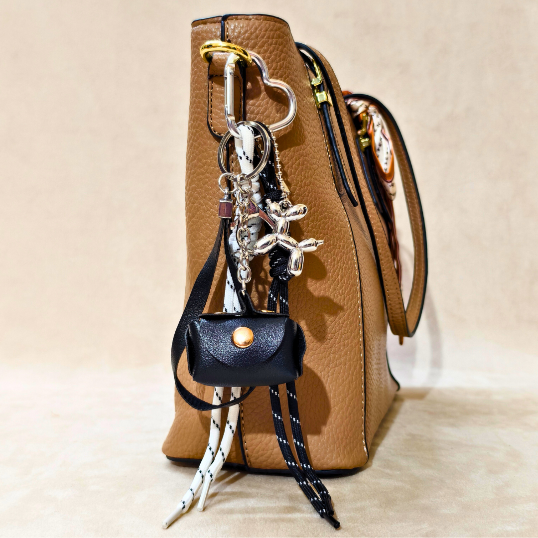Brown handbag with a black purse-shaped keychain and decorative elements on a beige background