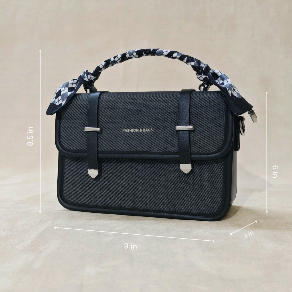 A black sling bag in front of fa beige background tilted over slightly to the left.