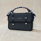 A black sling bag in front of fa beige background tilted over slightly to the left.