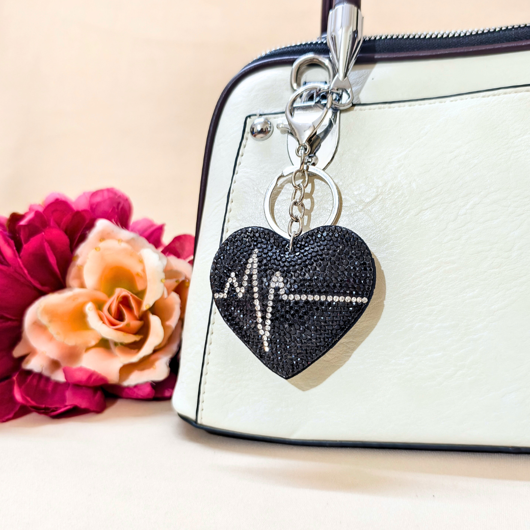 Black heart keychain placed on a purse beside a flower decoration in front of a beige background