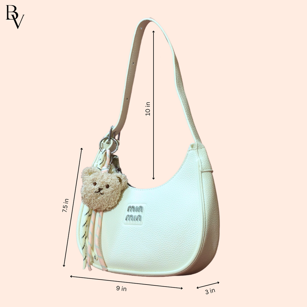 Light blue handbag with teddy bear charm and measurements on a pink background